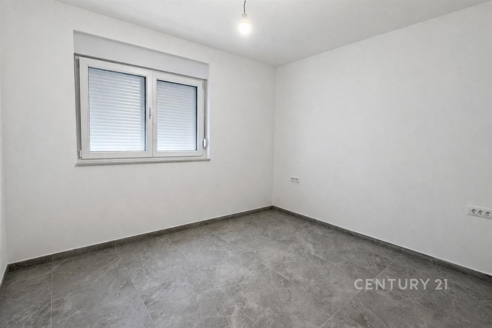 Prázdná místnost s šedou dlažbou, bílými stěnami a velkými okny, moderní a světlý design vytváří pocit prostornosti.
