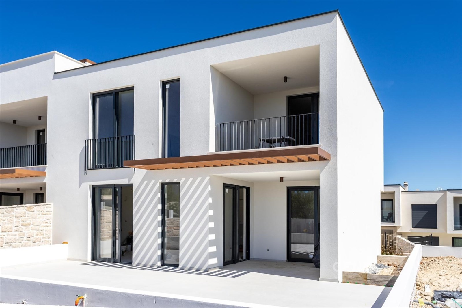 Moderní rodinný dům s velkými okny, minimalistickou fasádou a balkonem, který nabízí prostornou terasu s výhledem na zahradu.