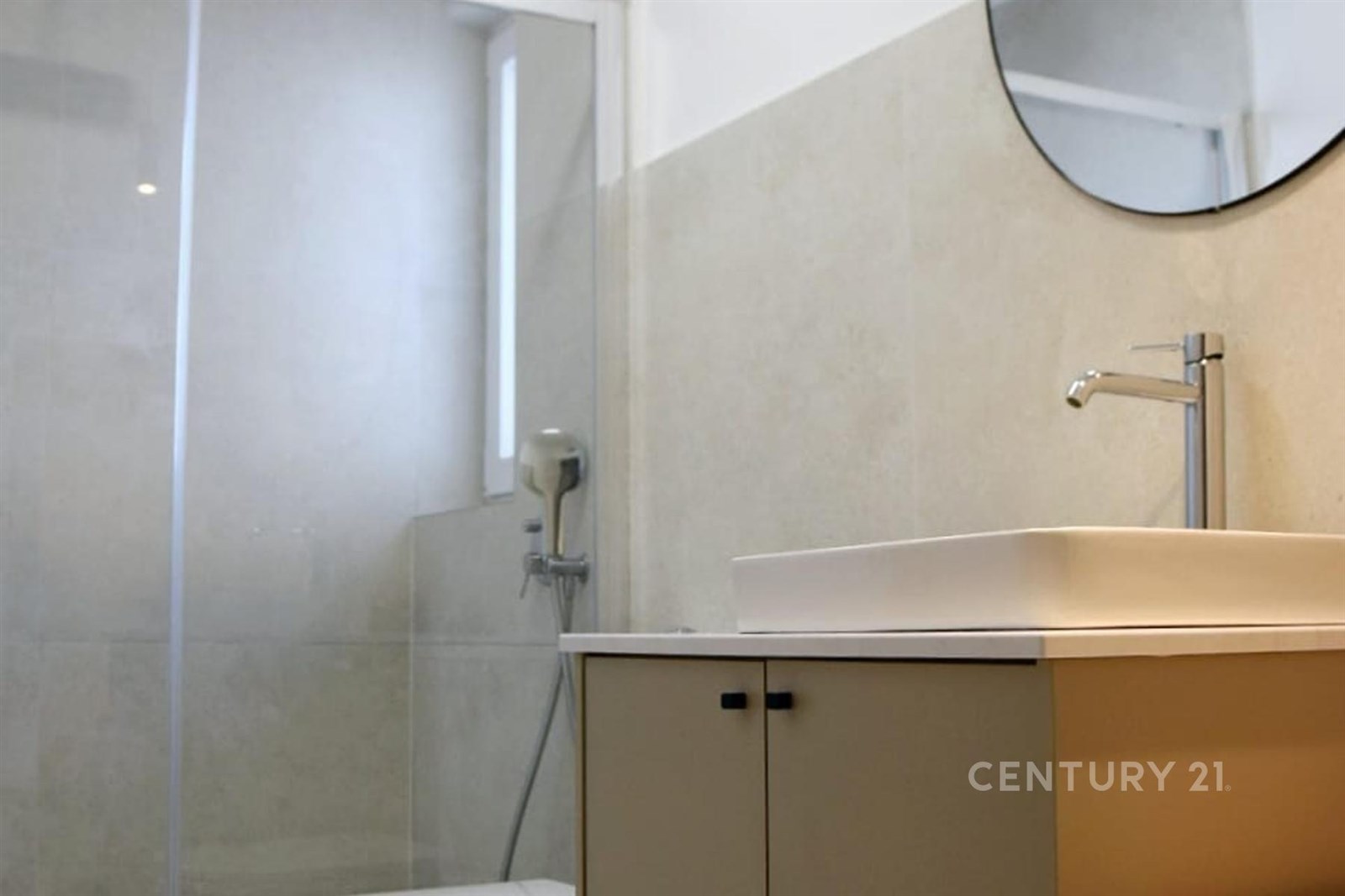 Moderní koupelna s velkými obklady, skleněným sprchovým koutem a elegantním umyvadlem, čisté a vkusné provedení.