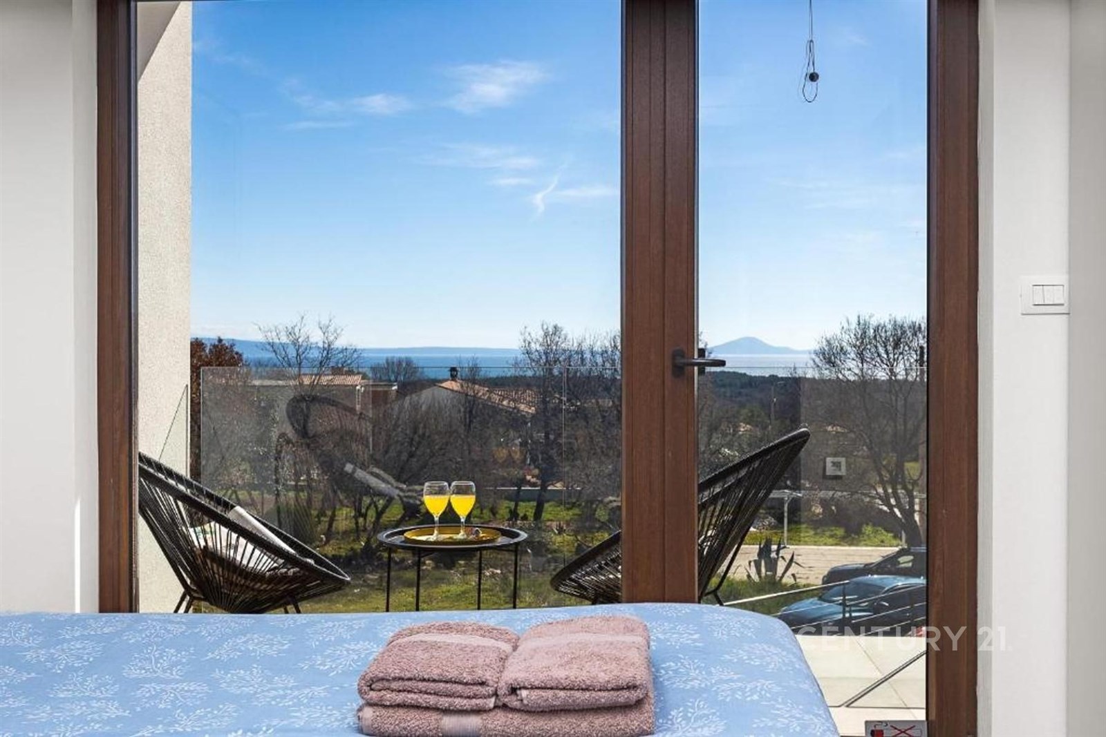 Výhled z ložnice s moderními okny a balkonem, nabízí panoramatický pohled na moře, doplněný stylovým nábytkem a minimalistickým dekorem.