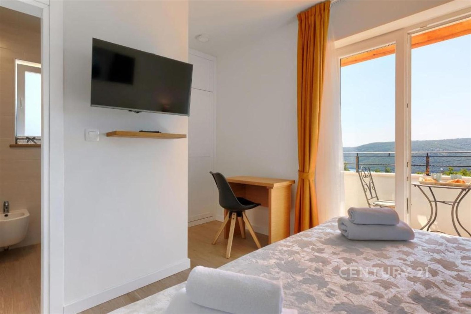 Světlá ložnice s moderní výbavou, parketová podlaha a velká okna vedoucí na balkon s výhledem na krajinu, ideální pro relaxaci.