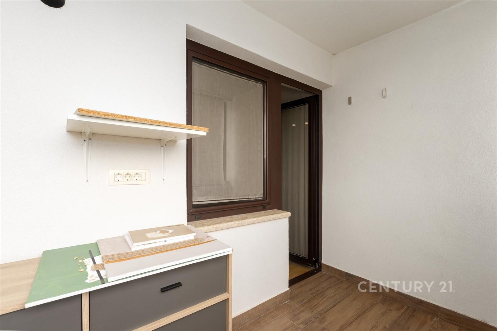 Malá předsíň s dřevěnou podlahou, bílými stěnami a velkým oknem. V prostoru se nachází moderní úložná skříňka.
