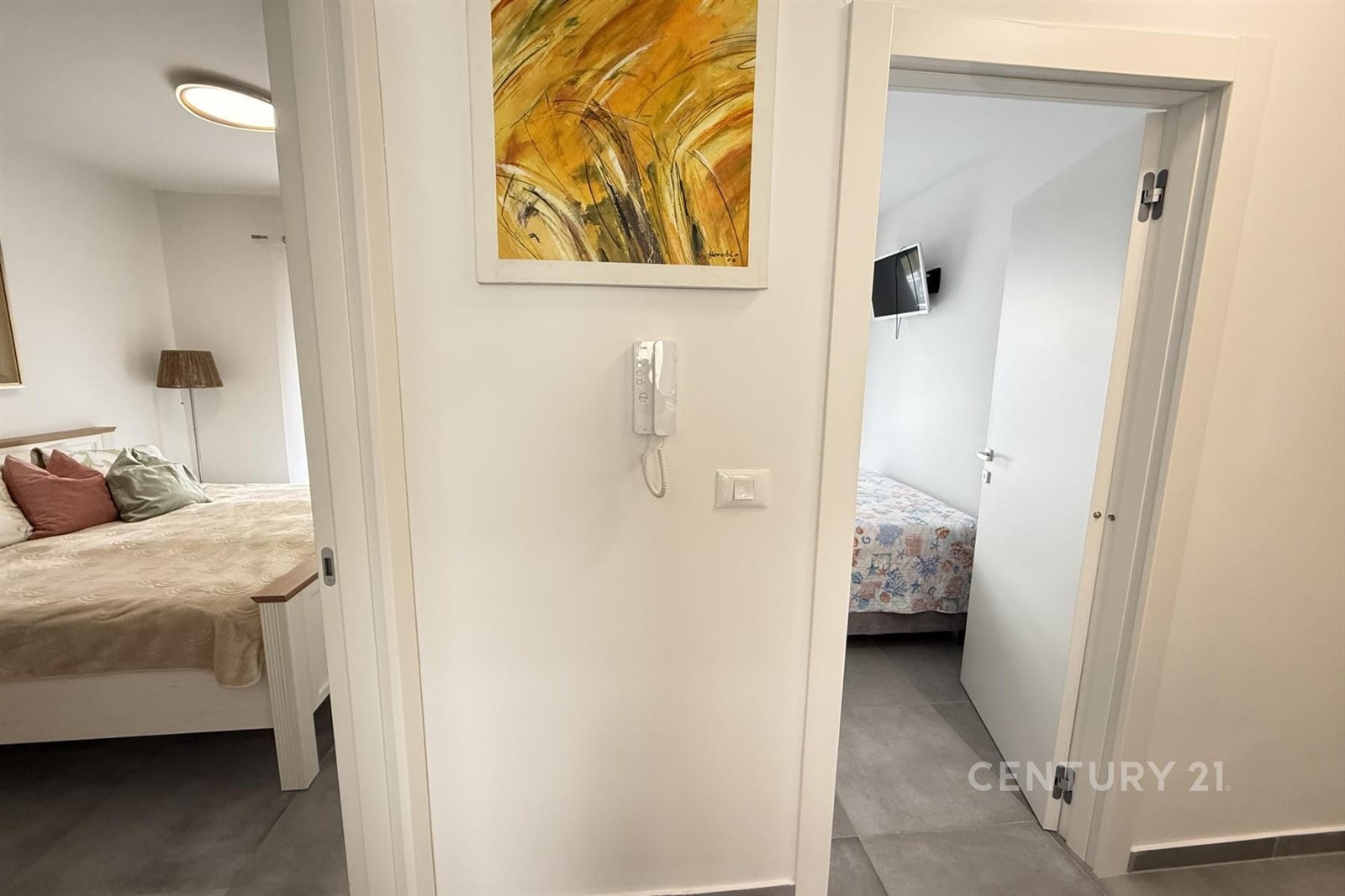 Světlá chodba s moderní dlažbou, accessem do ložnic s velkými okny a rekonstruovaným interiérem, stěny zdobí umělecké obrazy.
