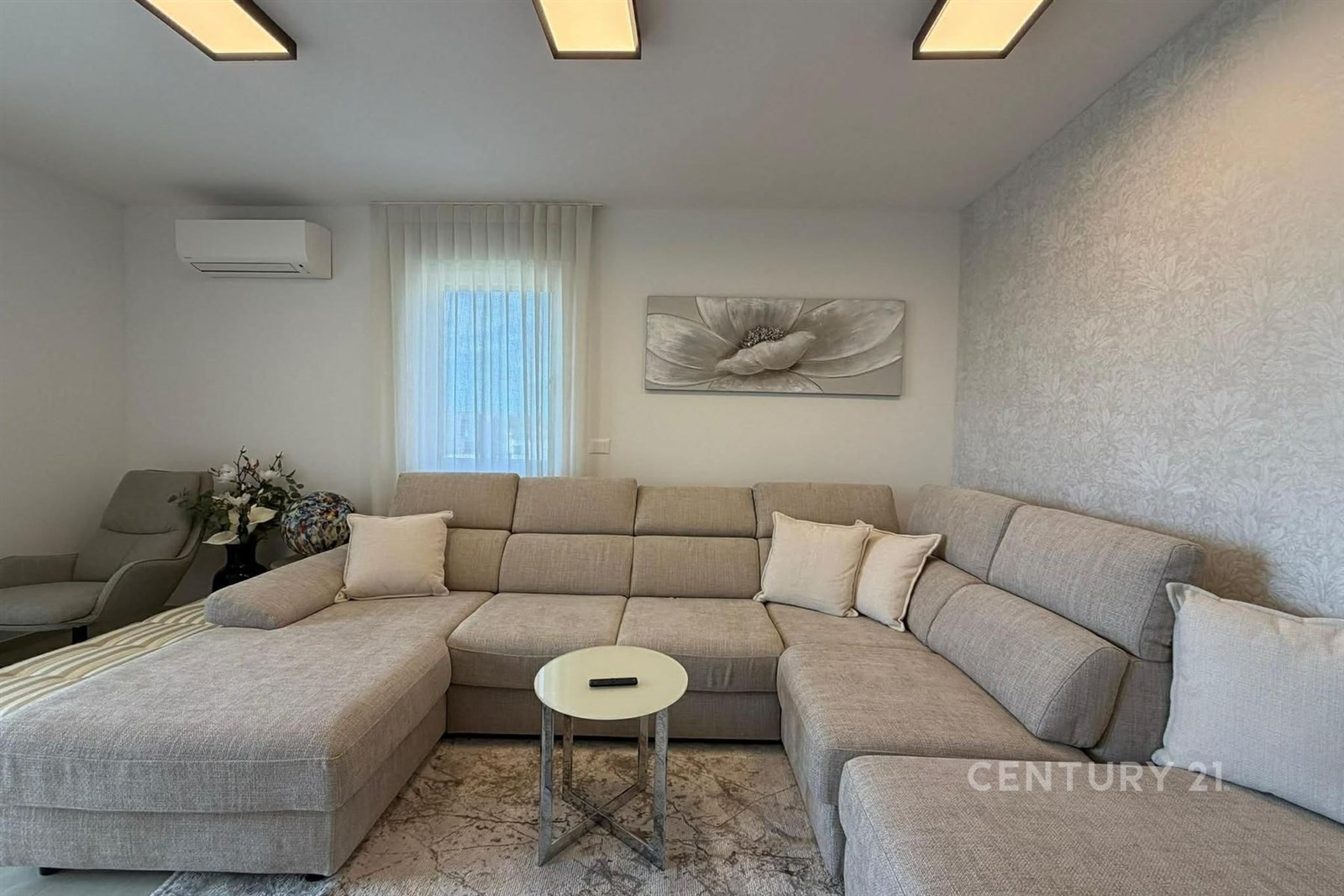 Světlý obývací pokoj, moderní design, velká sedací souprava, dekorativní tapeta, klimatizace, množství přírodního světla, pohodlný interiér.