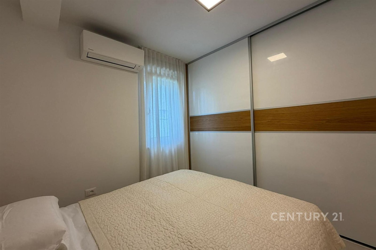 Světlá ložnice s vestavěnými skříněmi, moderní klimatizací a velkým oknem, které dodává prostoru vzdušnost a komfort.