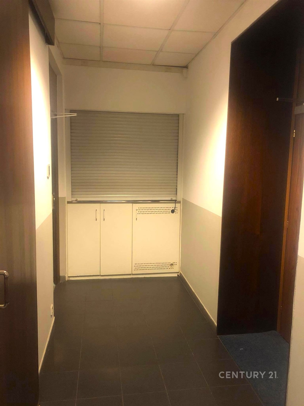 Úzká vstupní chodba s dlažbou, bílé stěny, vestavěné skříně a stropní osvětlení, moderní design, vhodné pro kanceláře.