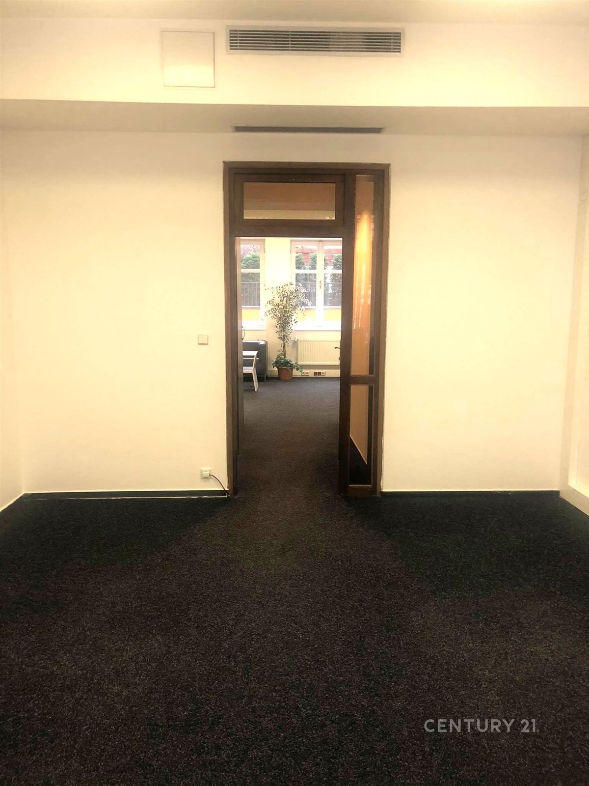 Průchod do světlé kanceláře s tmavým kobercem a velkými okny, moderní topný systém, minimalistický design.