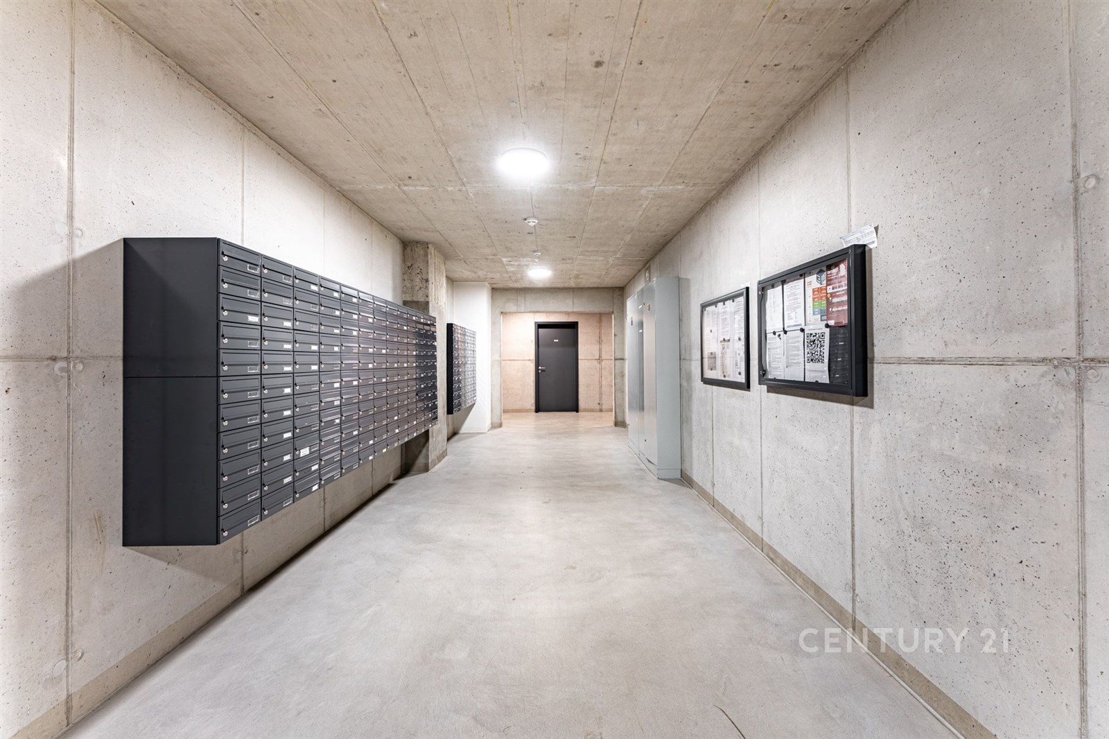 Společná chodba se světlou betonovou podlahou, černými poštovními schránkami a moderními osvětlením, působí čistým a minimalistickým dojmem.