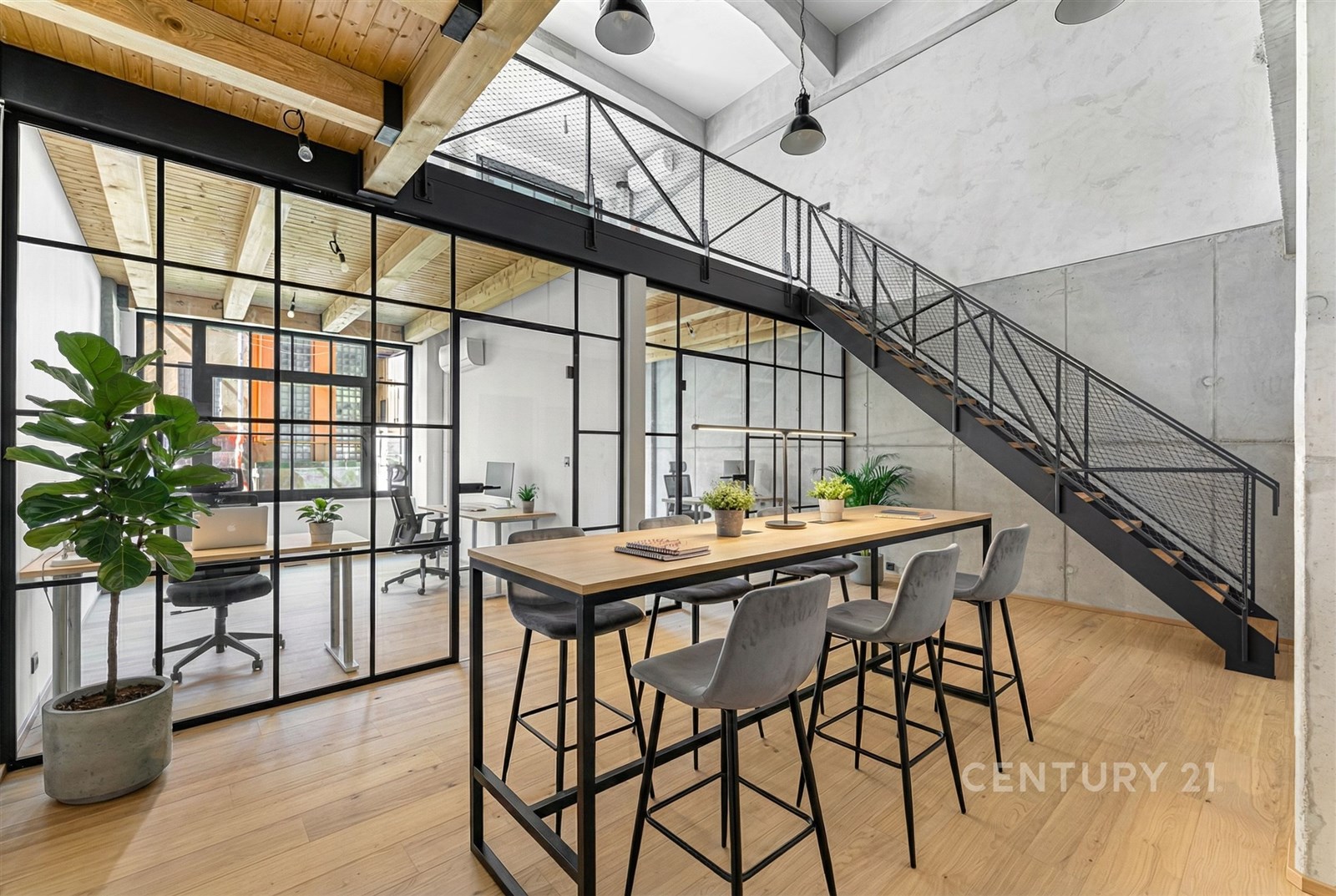Moderní kancelářský prostor s dřevěnou podlahou, skleněnými příčkami, a ocelovým schodištěm. Velká okna poskytují dostatek přirozeného světla.