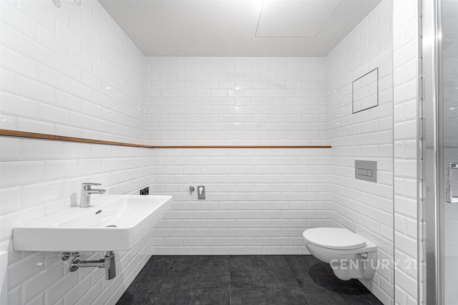 Moderní koupelna s bílými obklady, závěsnou toaletou a umyvadlem. Kombinace dlažby na podlaze a čistý design vytváří světlý prostor.