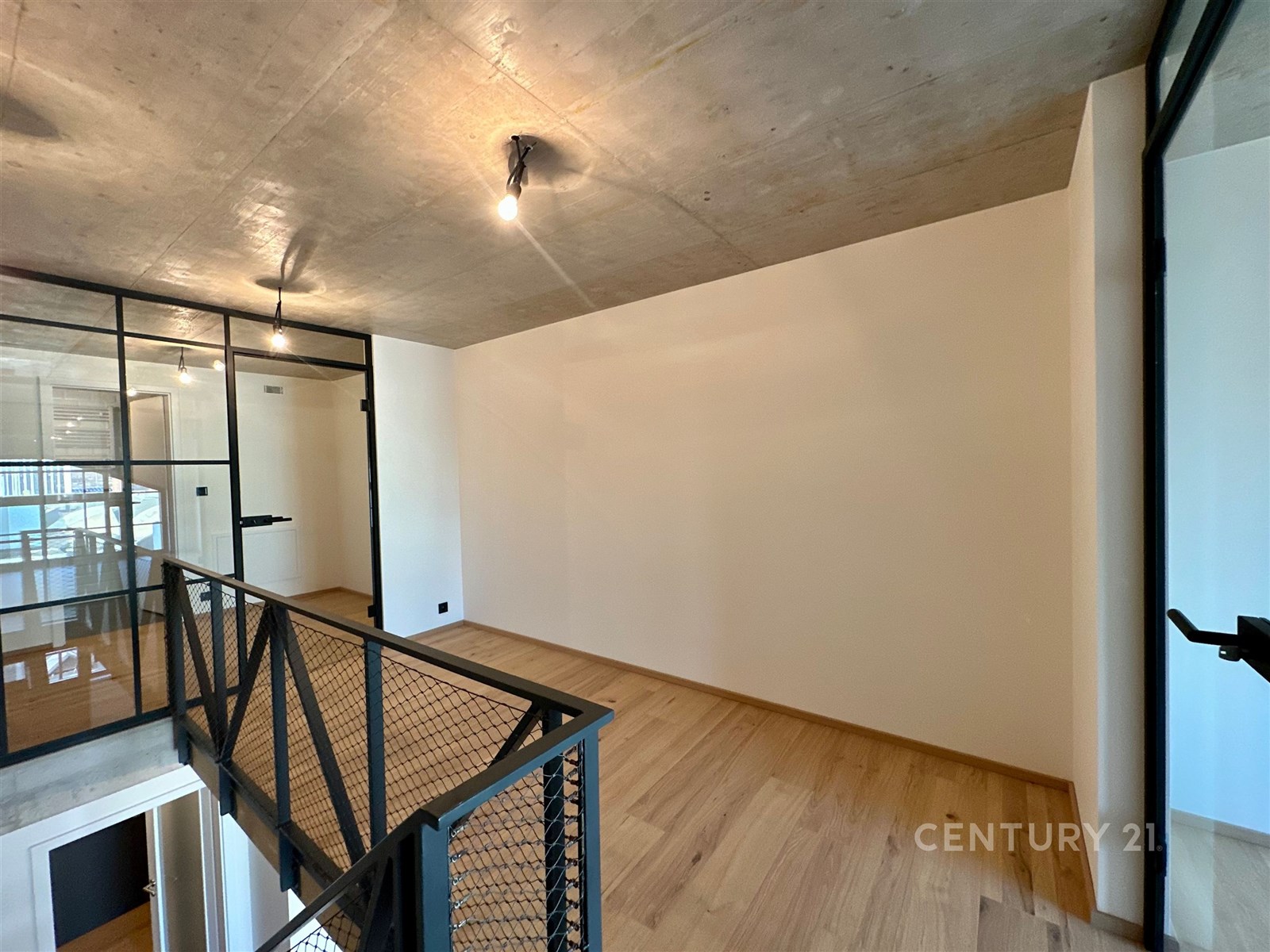 Prázdná pokoj s parketovou podlahou, moderní průmyslový styl, kovové zábradlí a betonový strop, ideální pro loftový design.