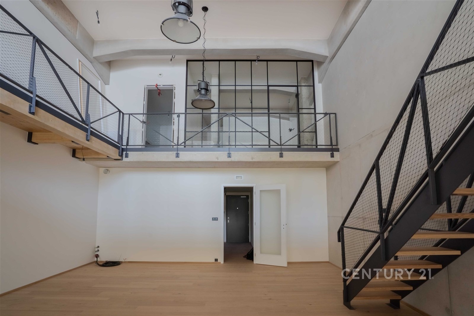 Světlý obývací pokoj s moderními prvky, parketová podlaha a velká okna, kovové schodiště do patra, industriální styl pro prostorný interiér.