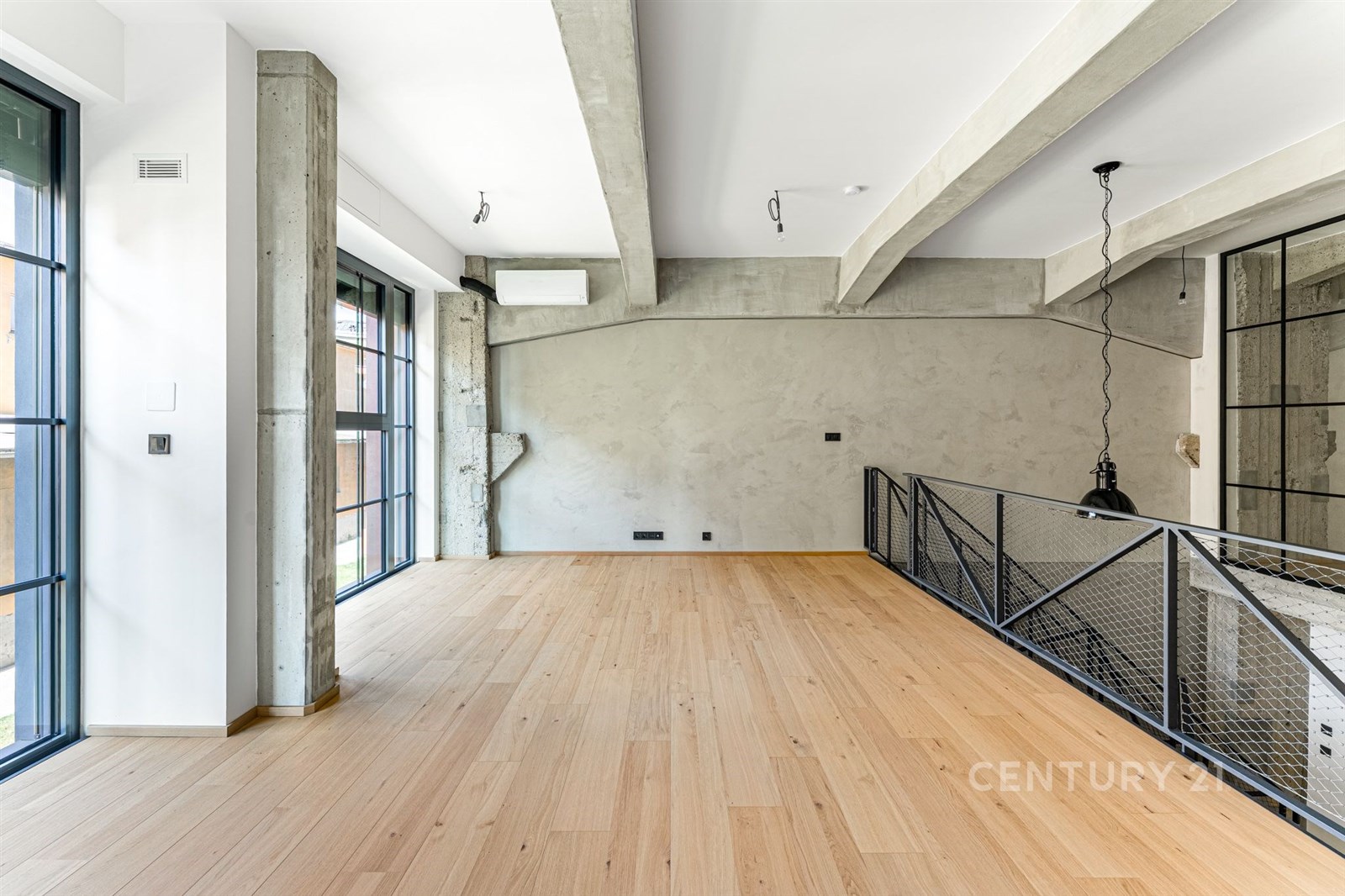 Moderní obývací pokoj s parketovou podlahou, velkými okny a industriálním stylem. Světlý prostor s betonovými trámy a minimalistickým designem.