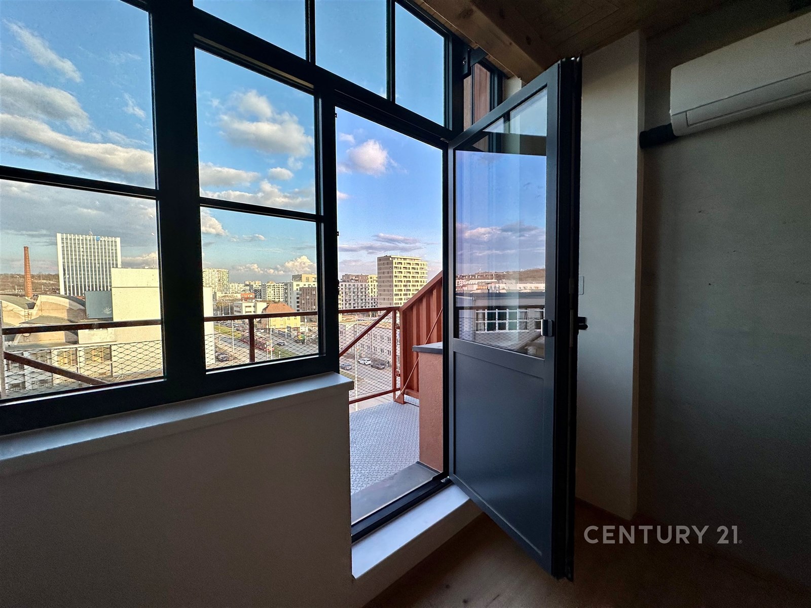 Balkon s velkými okny, parketovou podlahou a moderní klimatizací nabízí panoramatický výhled na město.