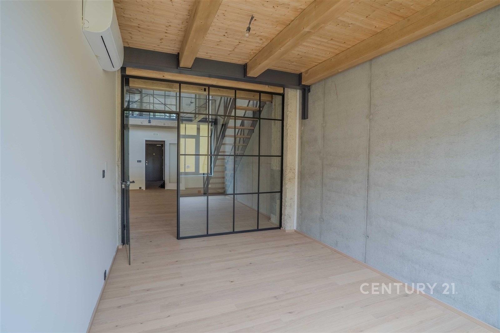 Průmyslově laděná místnost s parketovou podlahou, pohledovým betonem a skleněnými posuvnými dveřmi; moderní styl a klimatizace