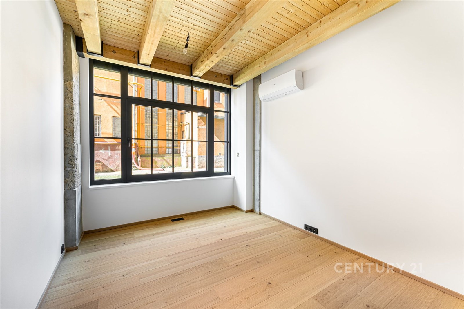 Pokoj s parketovou podlahou, dřevěný strop a velká okna. Moderní vzhled s klimatizací zajišťuje pohodlí a eleganci prostoru.