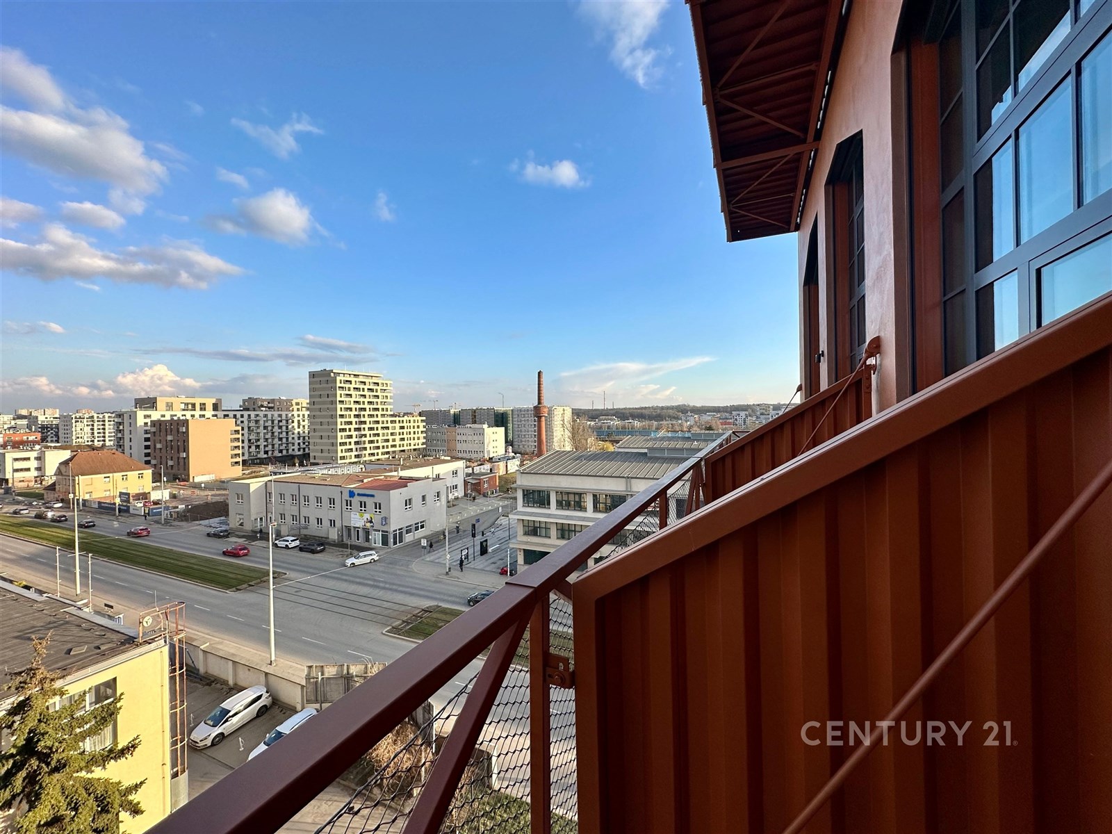 Výhled z balkonu s moderní konstrukcí, který nabízí panoramatický pohled na město, vhodný pro milovníky městského života.