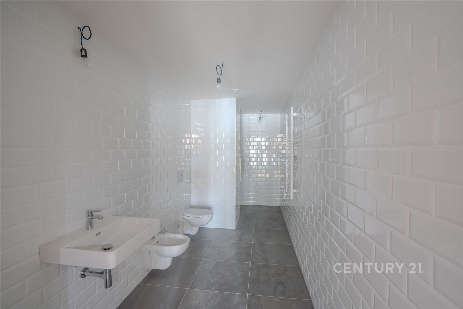 Koupelna s bílými obklady, moderními prvky a dlažbou, prostorná dispozice a minimalistický design.