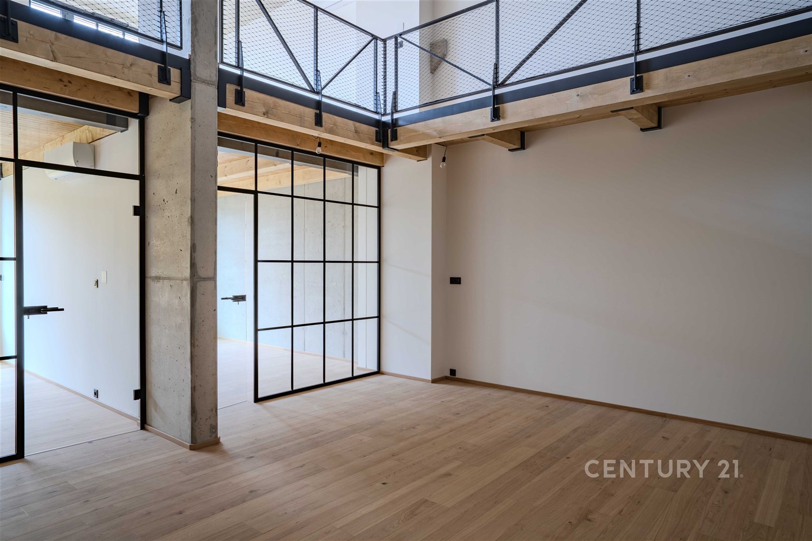 Prostorný obývací pokoj s parketovou podlahou, moderní skleněné dveře a ocelové prvky, světlý interiér s vysokým stropem.