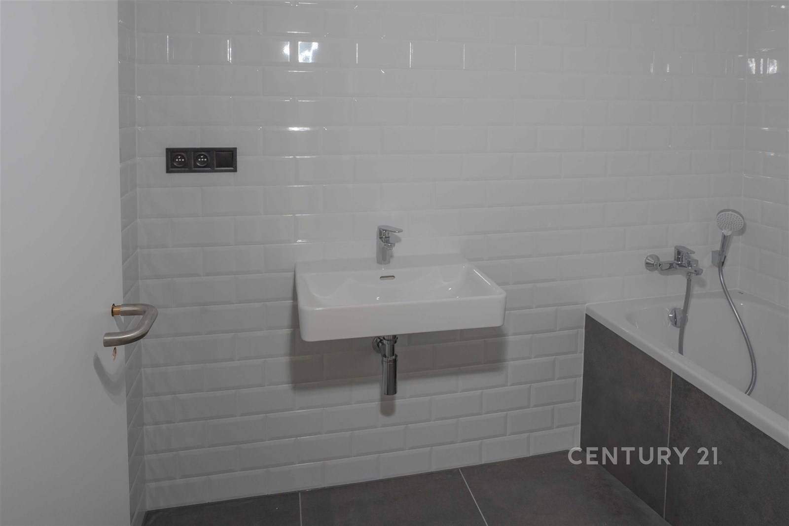 Moderní koupelna s bílou dlažbou, šedými obklady a vanou, vybavená umyvadlem a chromovými doplňky