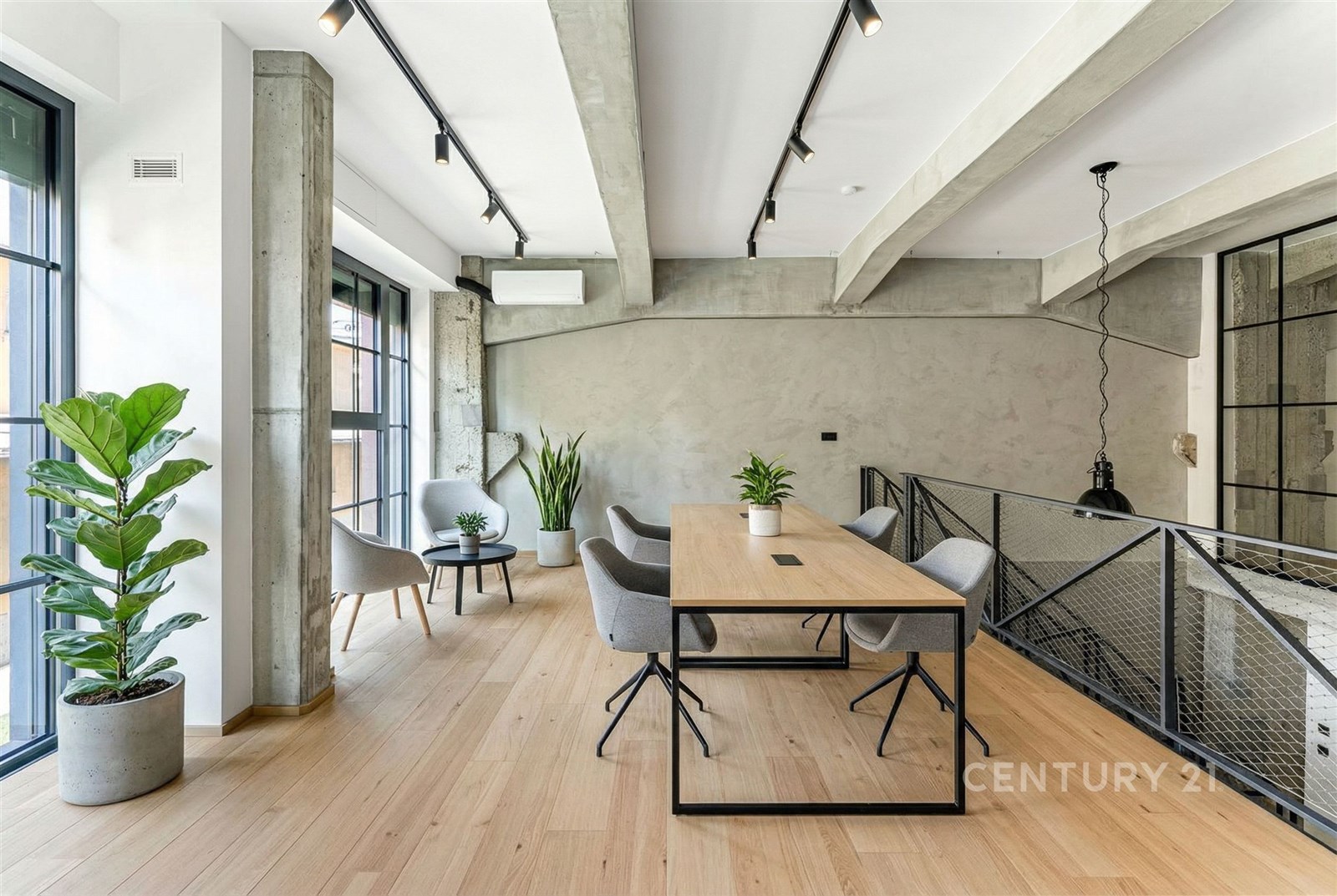 Moderní pracovní prostor s parketovou podlahou, velkými okny a industriálním designem. Elegantní nábytek a květiny dodávají světlou atmosféru.