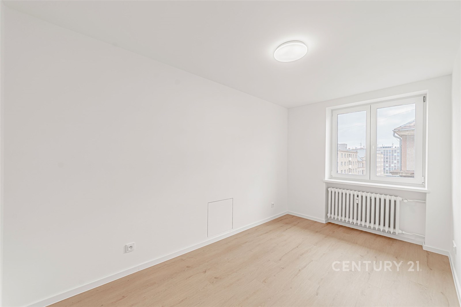 Světlý pokoj s dřevěnou podlahou, velkým oknem a b