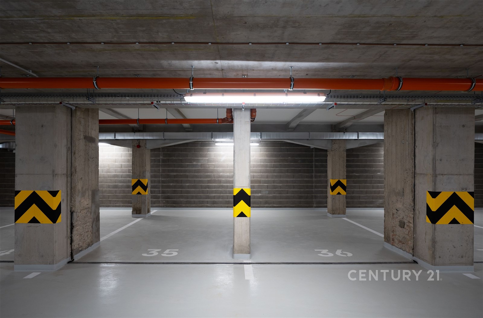 Prázdné parkovací místo v moderní garáži s betonovou podlahou, sloupky s bezpečnostním značením, dobré osvětlení, bezpečné prostředí.