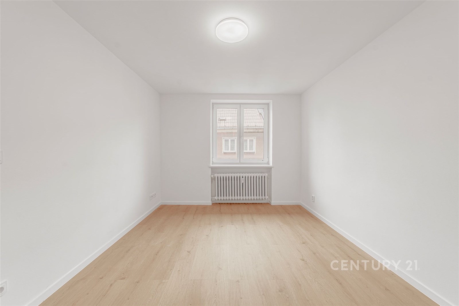 Světlý pokoj s parketovou podlahou, velkým oknem a