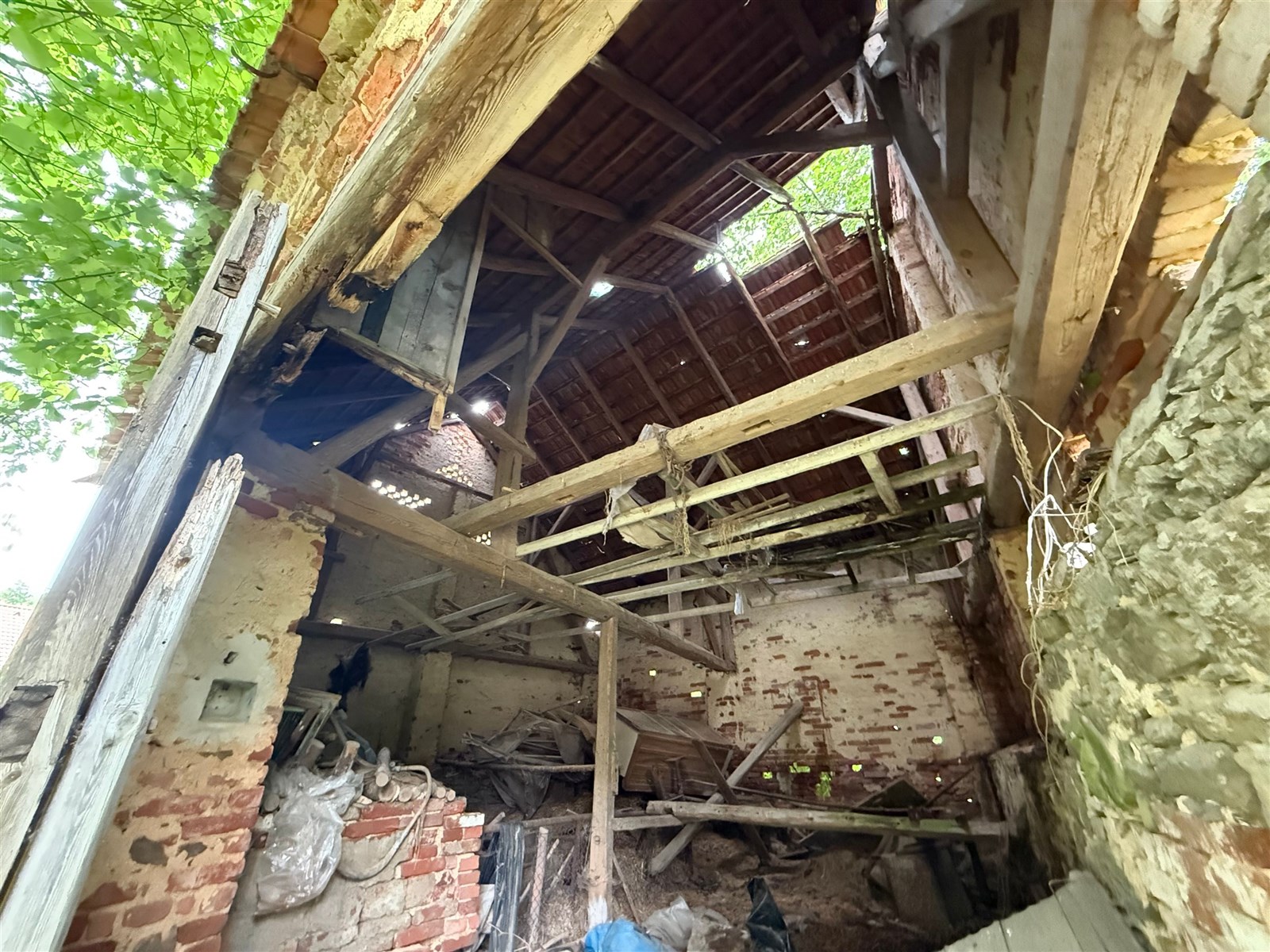 Starý hospodářský prostor s cihlovými zdmi, dřevěnými trámy a poškozenou střechou, vhodný k rekonstrukci nebo demolici.