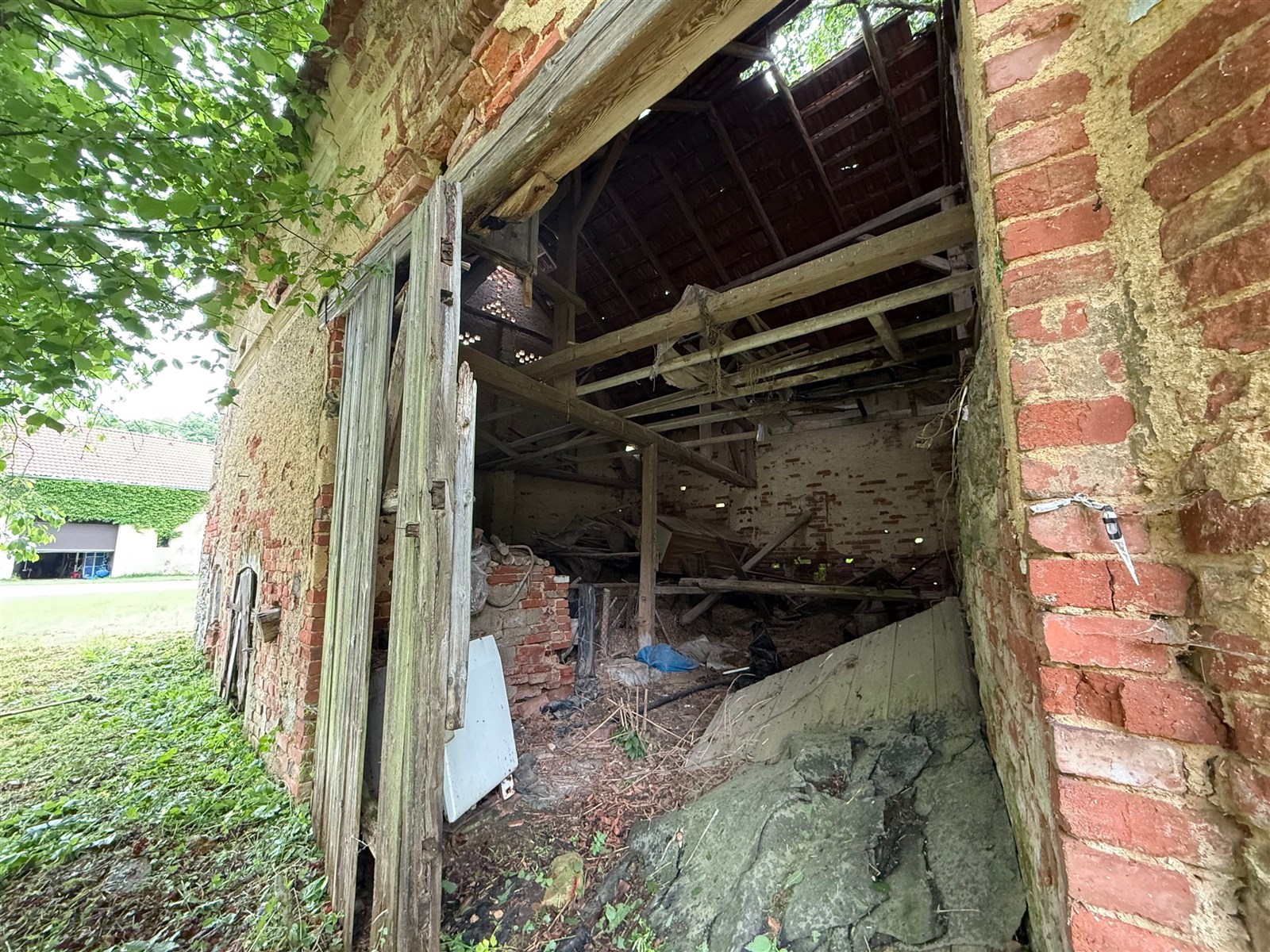 Zchátralá stodola s cihlovými zdmi a rozpadlou střechou, vhodná k rekonstrukci na venkovském pozemku.