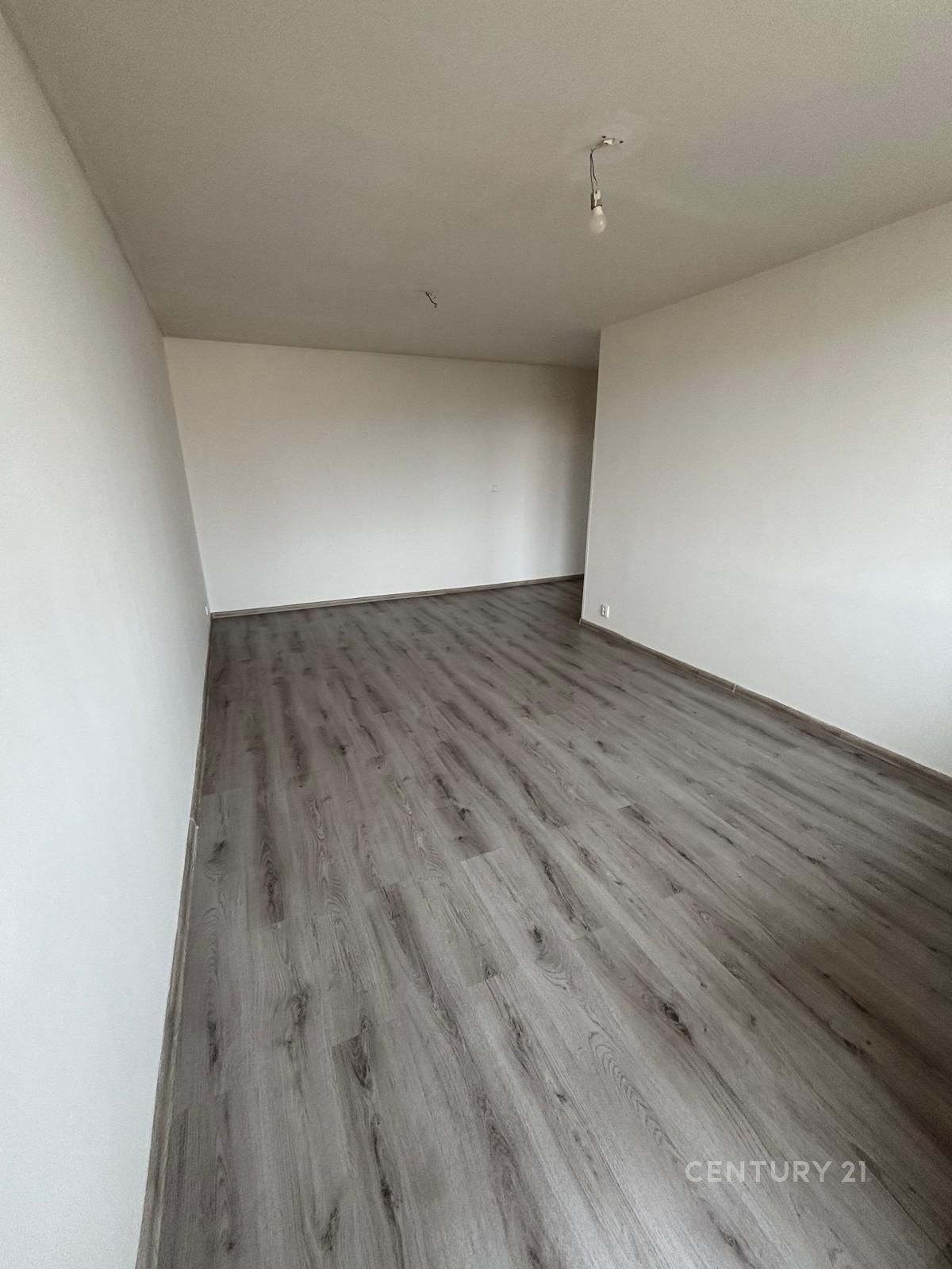 Prázdný obývací pokoj s moderní vinylovou podlahou, bílými stěnami a minimalistickým stylem, ideální pro vlastní úpravy.