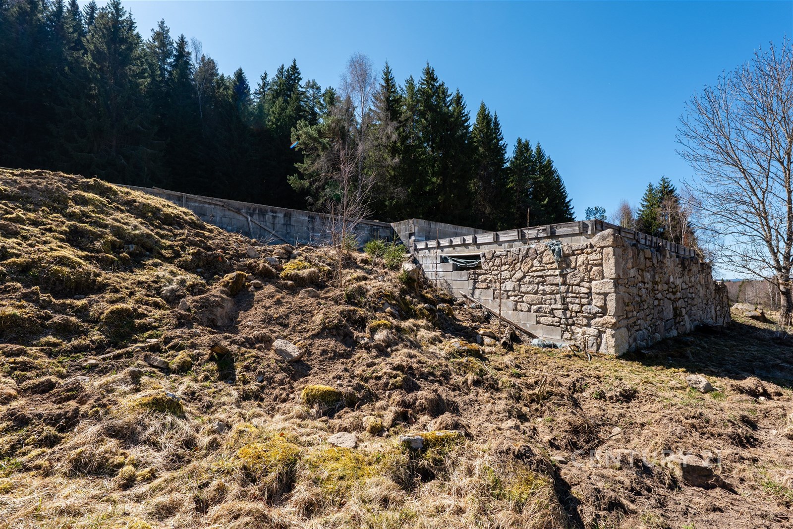 Kamenná opěrná zeď obklopená přírodní krajinou, s 