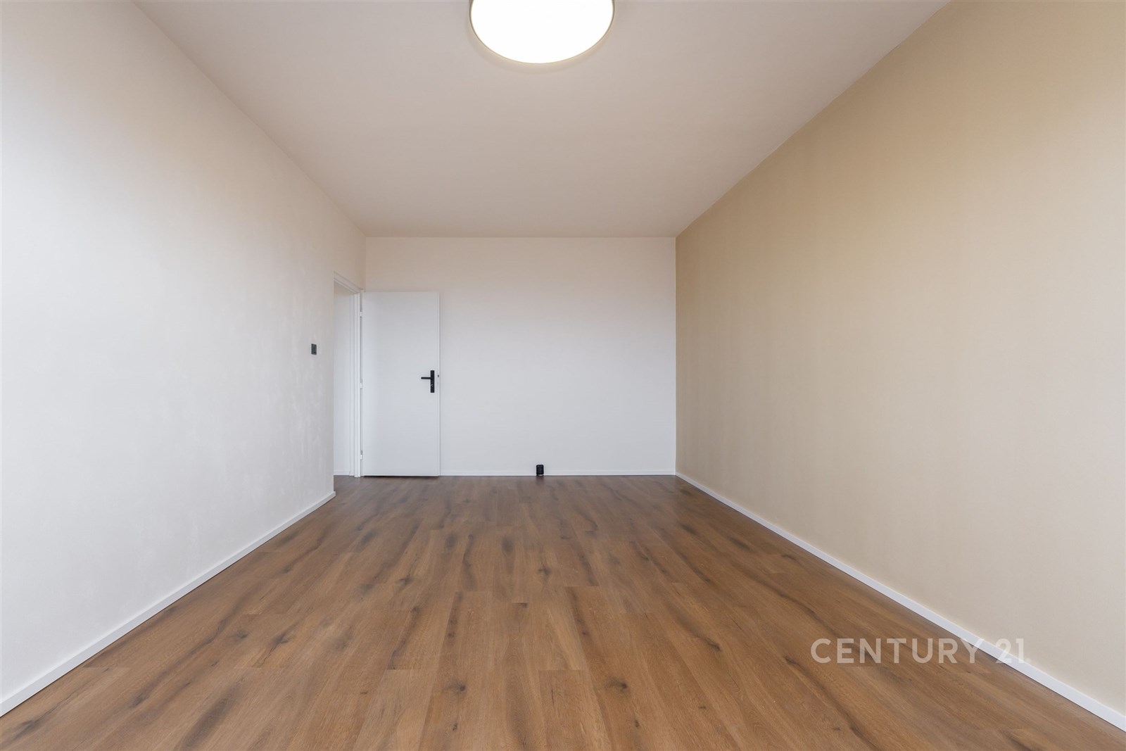 Úzká místnost s parketovou podlahou, světlé stěny,