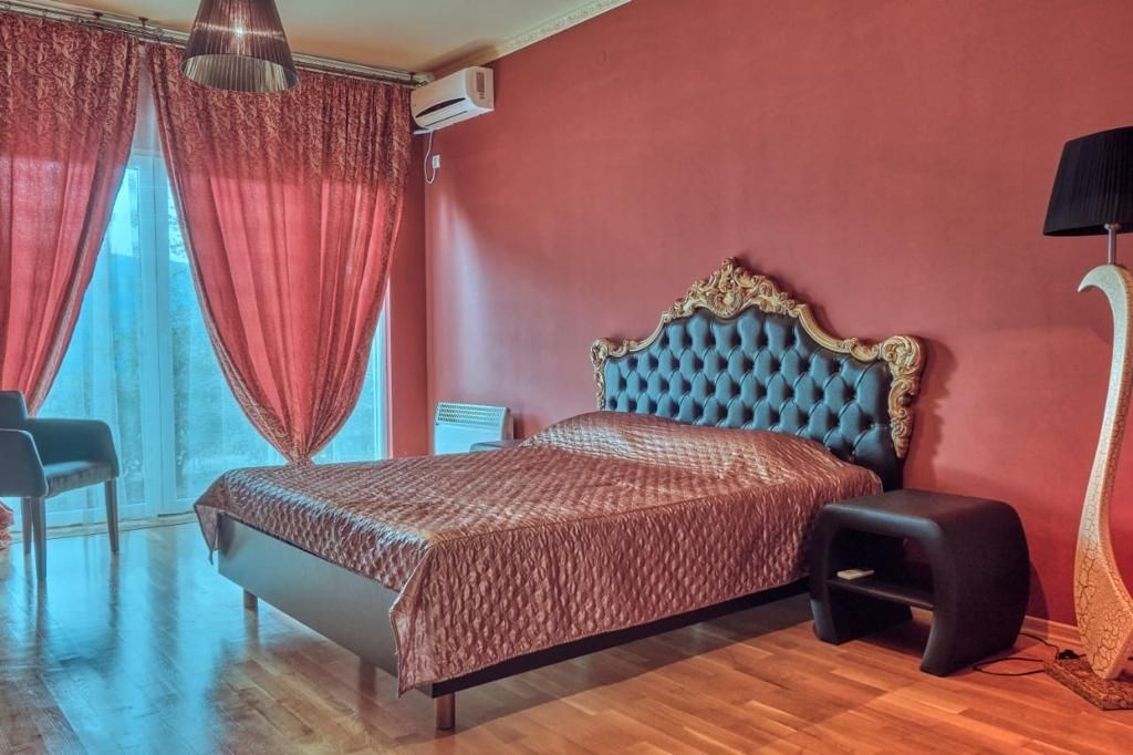 Prostorná ložnice s luxusní čalouněnou postelí, parketovou podlahou a velkými okny poskytujícími dostatek světla