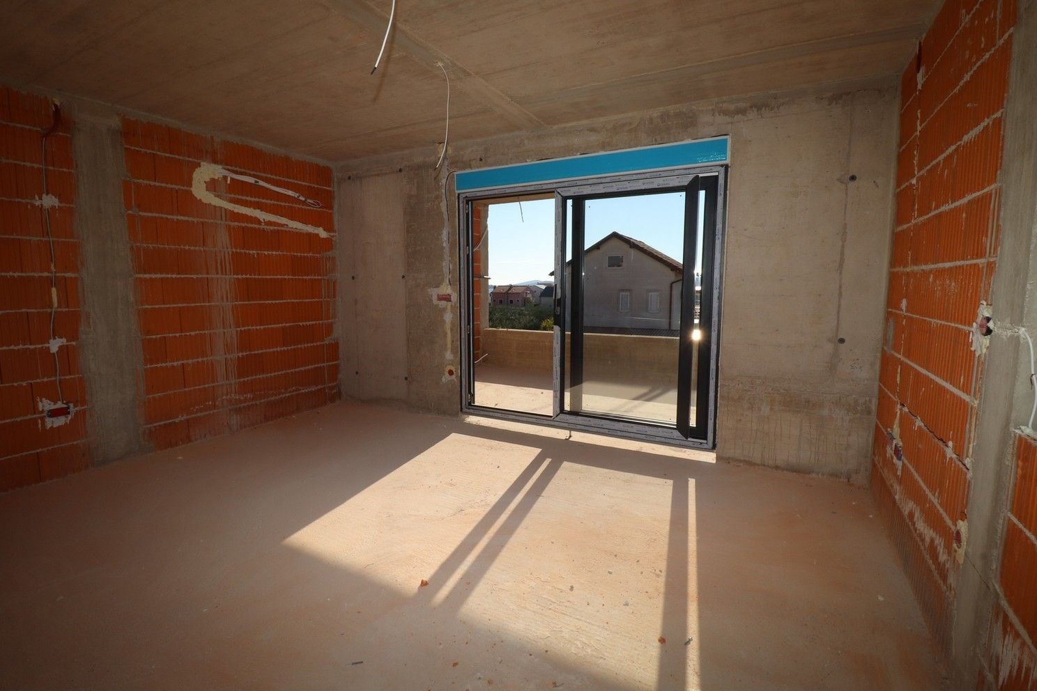 Nezařízený obývací pokoj s velkými okny, betonovými stěnami a surovým betonovým stropem, ideální pro moderní rekonstrukci.