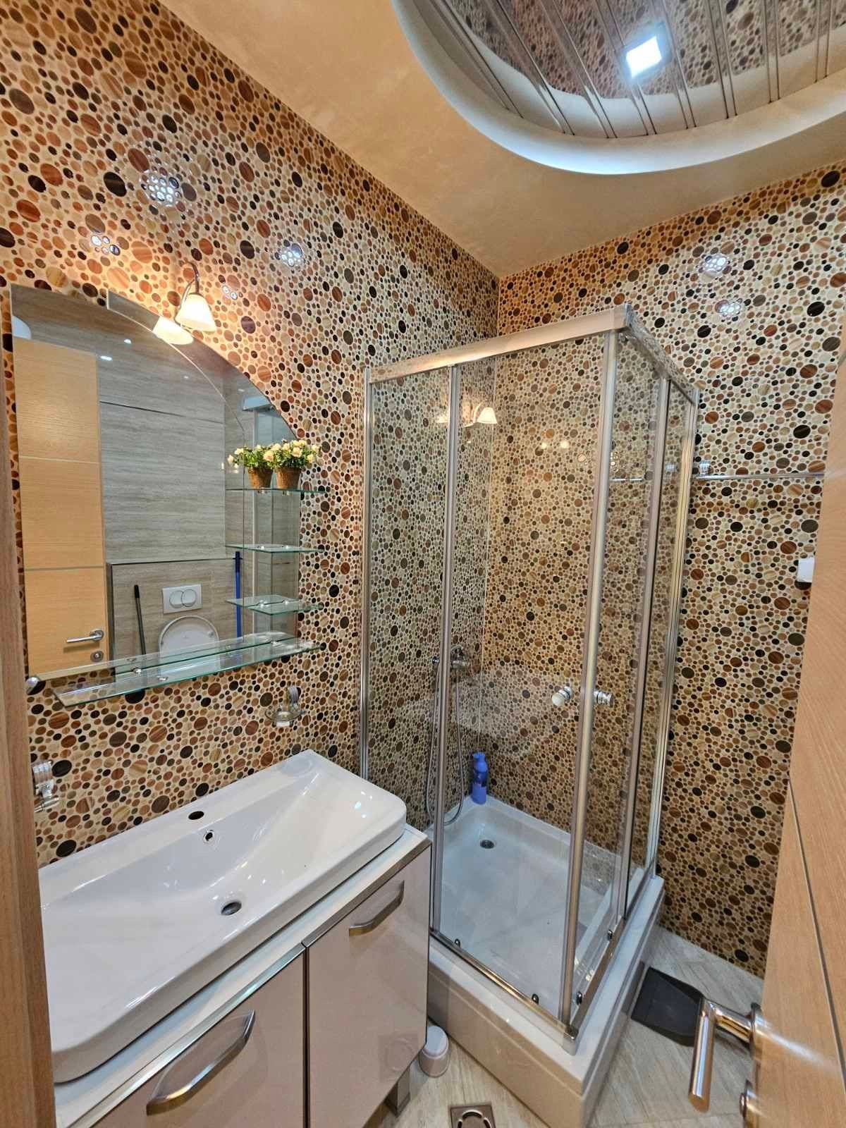 Koupelna s mozaikovými obklady, moderním sprchovým koutem a závěsným umyvadlem, světlé dřevo na podlaze poskytuje elegantní vzhled.