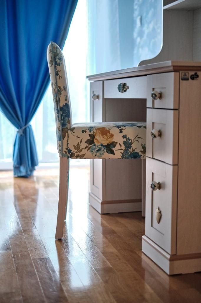 Pracovní kout s dřevěnou podlahou a elegantním psacím stolem, doplněný o křeslo s květinovým vzorem a velkými okny pro maximální světlost.
