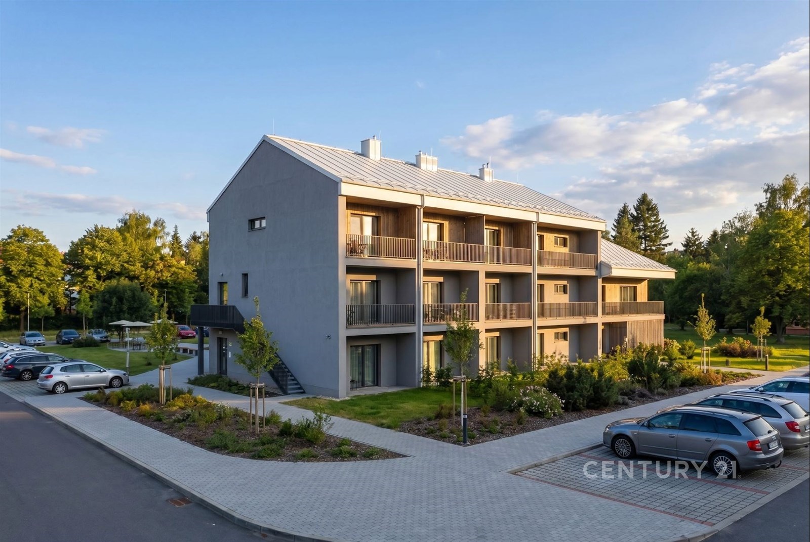 Moderní bytový dům s balkony, kvalitní fasádou a upraveným parkovištěm, nacházející se v klidné lokalitě obklopené zelení.