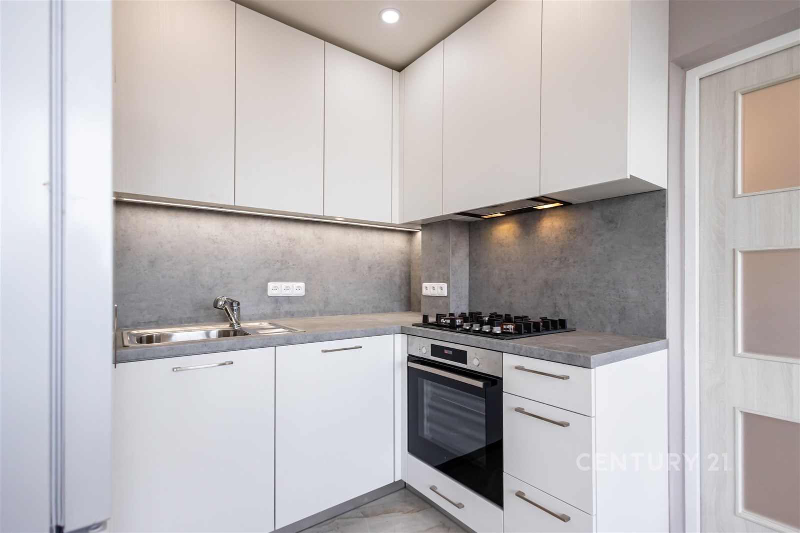 Moderní kuchyň s bílými skříňkami, šedou pracovní deskou a vestavěnou troubou, elegantní design a praktické osvětlení pod linkou