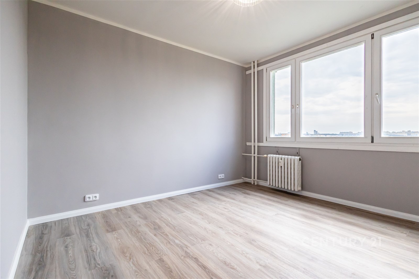 Světlý pokoj s velkými okny, moderní laminátová podlaha, neutrální výmalba.