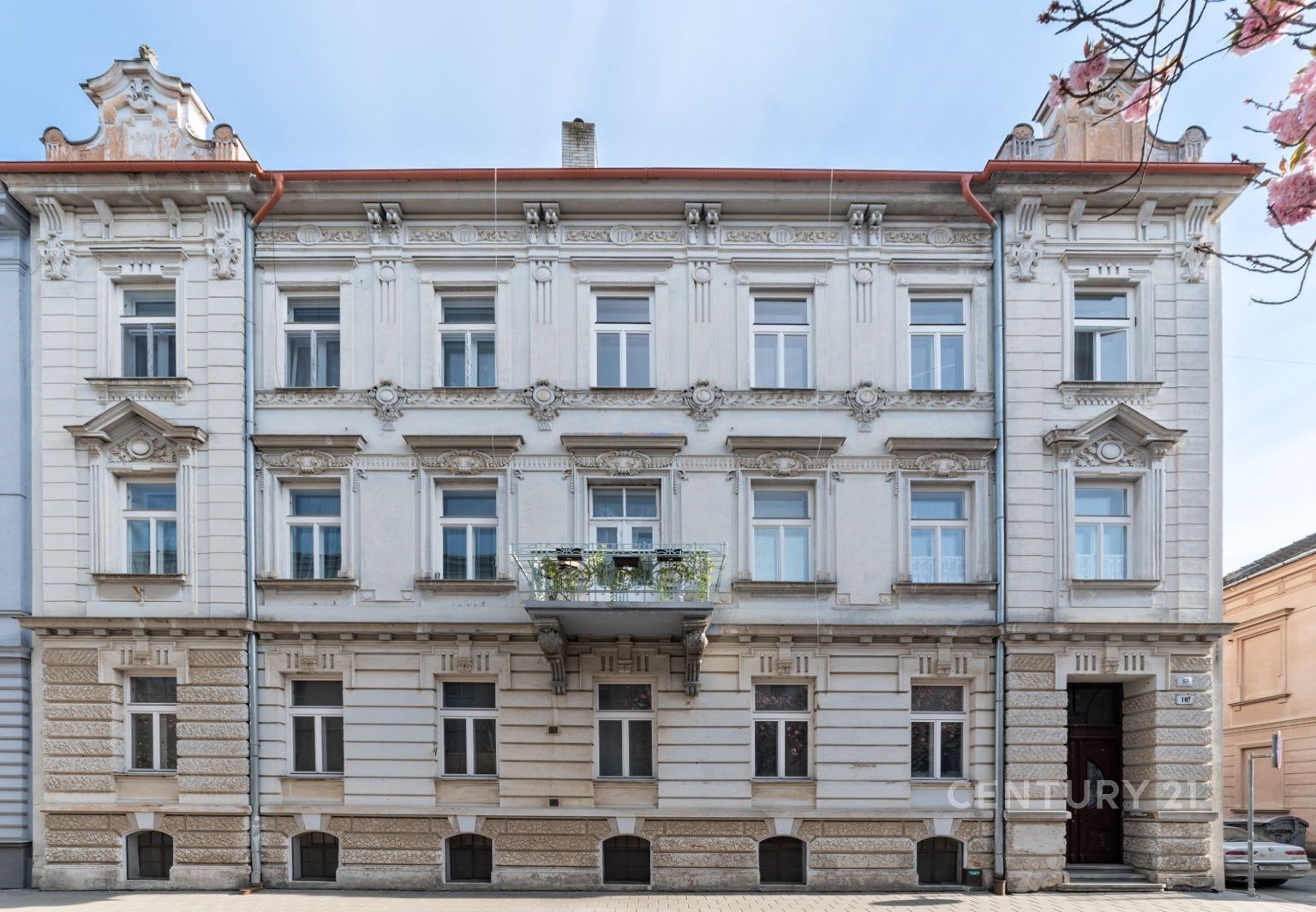 Historická budova s dekorativní fasádou a balkonem, zdobené detaily a udržovaný vchod, ideální pro městské bydlení.