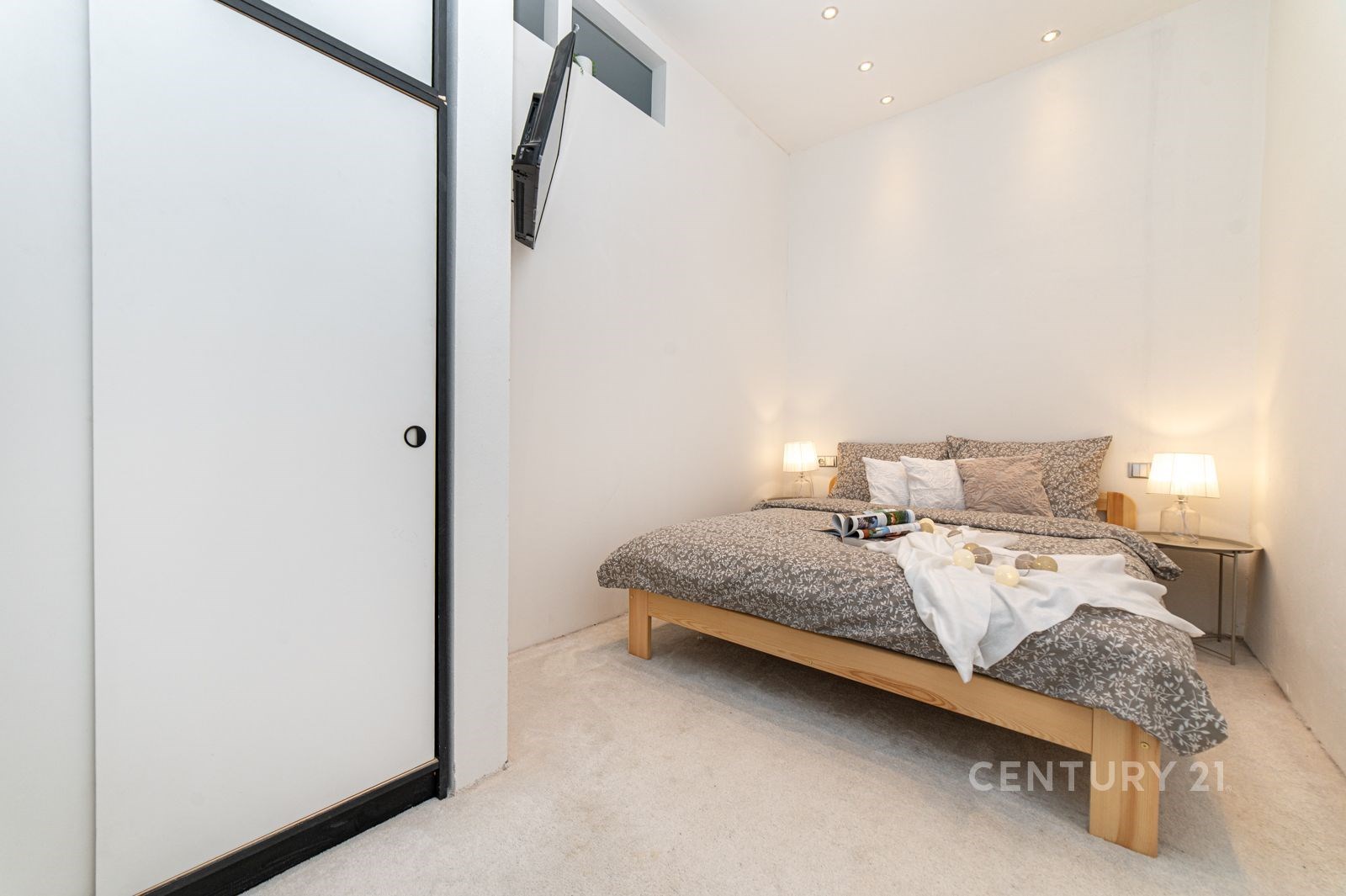 Světlá ložnice s moderním designem, vestavěné skříně, světlý koberec a minimalistické osvětlení vytváří útulnou atmosféru.