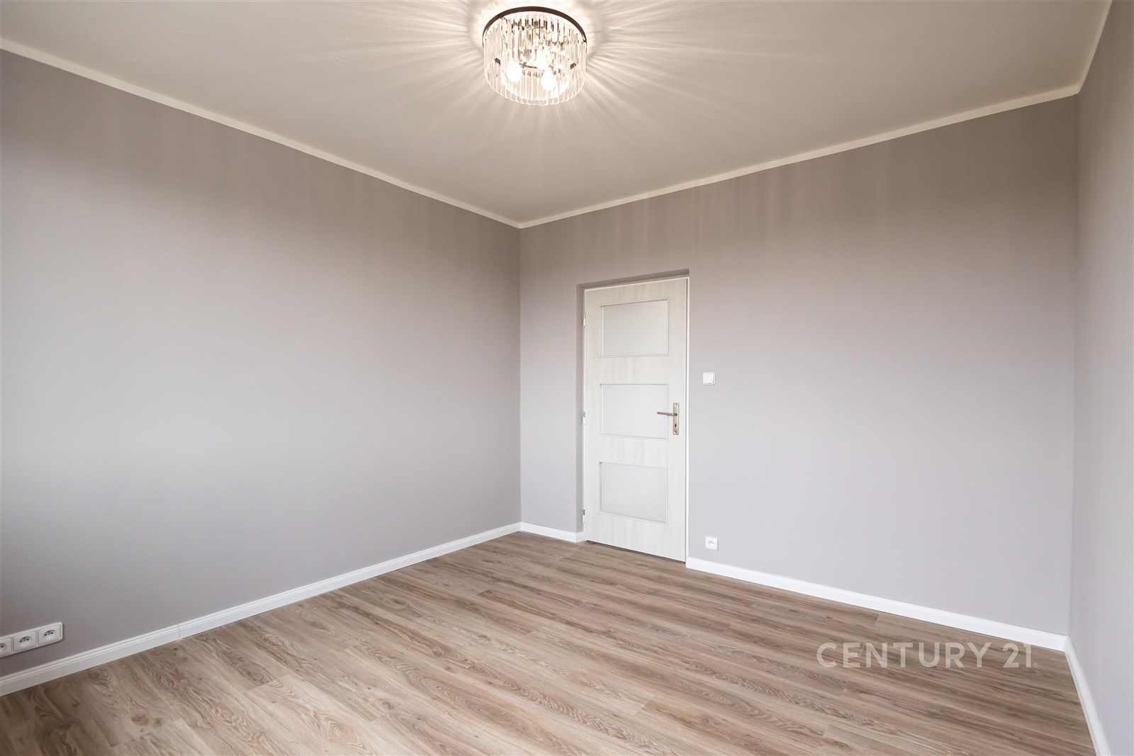 Prázdná místnost s parketovou podlahou, moderním osvětlením a světlými stěnami, ideální pro přizpůsobení podle vlastního stylu.