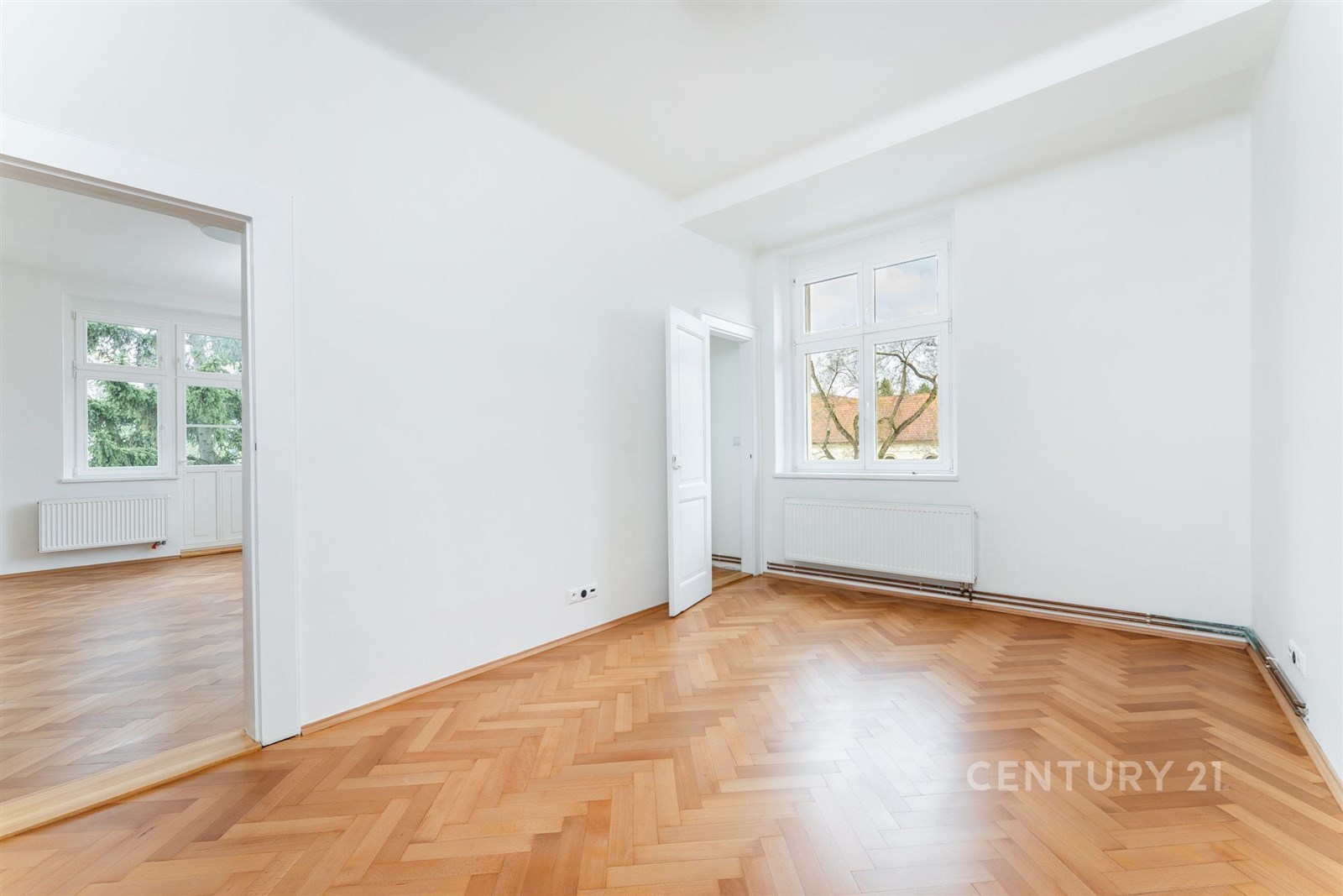 Světlý pokoj s parketovou podlahou a velkými okny,