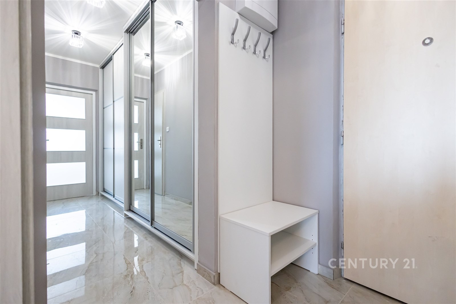 Chodba s dlažbou, velkými zrcadlovými posuvnými dveřmi a moderním osvětlením. Stěny v světlém provedení vytvářejí prostorný dojem.