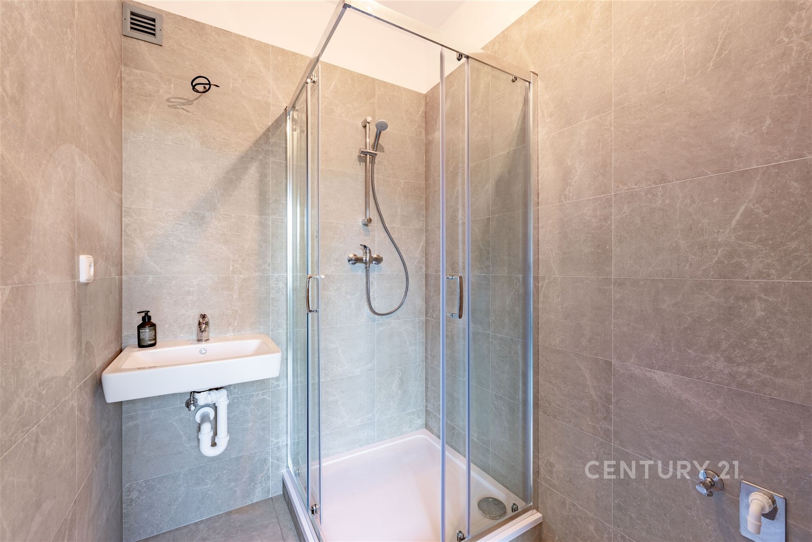 Moderní koupelna s keramickými obklady, sprchovým koutem a nástěnným umyvadlem, elegantní design a snadná údržba.