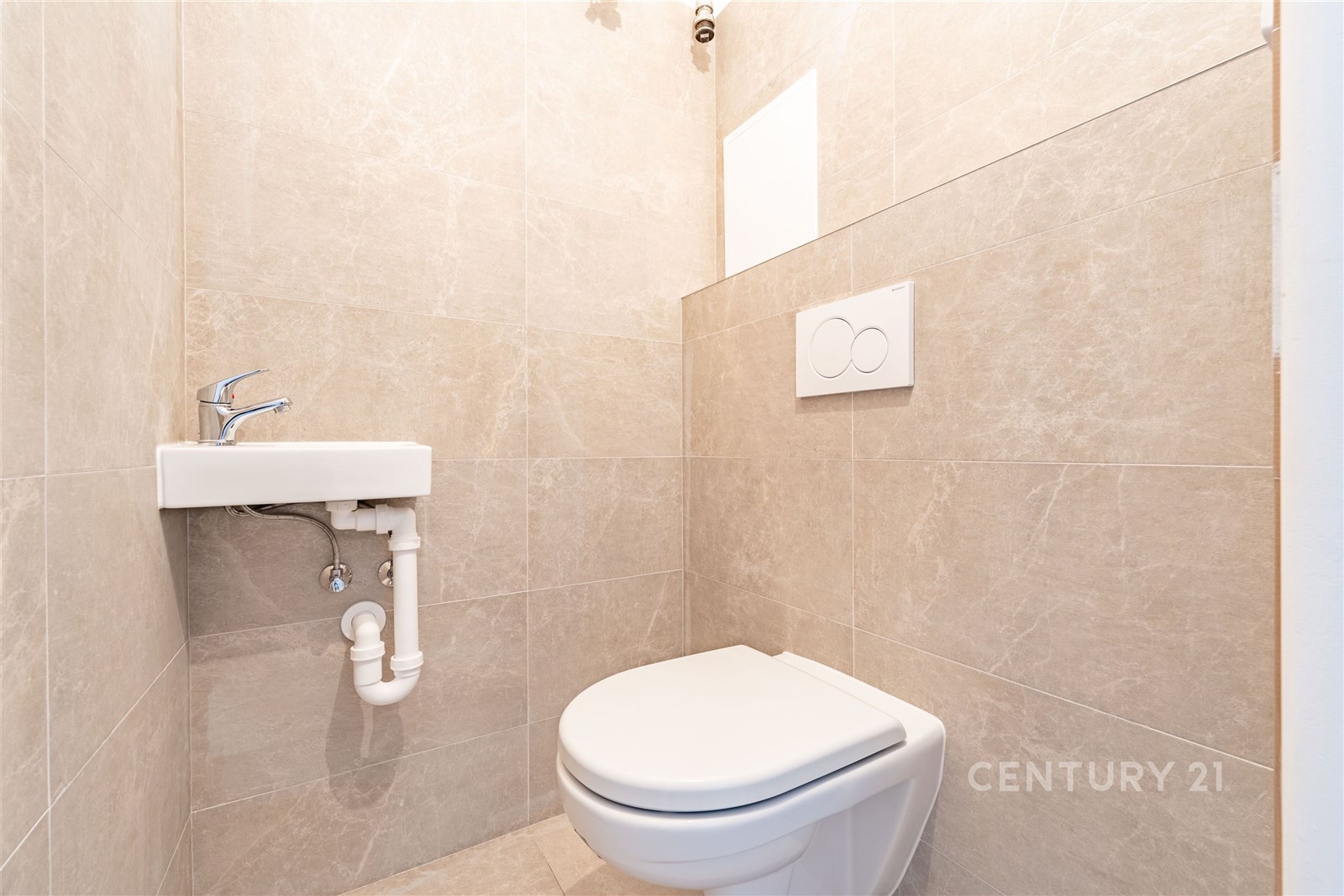 Moderní toaleta s dlažbou, bílým závěsným wc a malým umyvadlem, světlé stěny a minimalistický design.