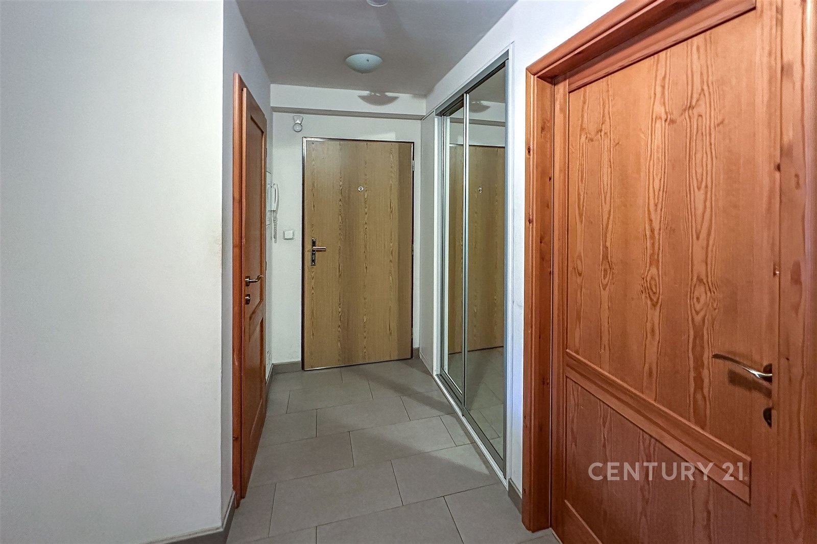 Chodba s dlažbou, vestavěnými skříněmi a dřevěnými dveřmi nabízí moderní vzhled a praktické úložné řešení.