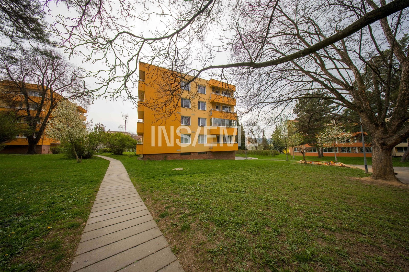 Čtyřpatrový panelový dům se žlutou fasádou, obklop