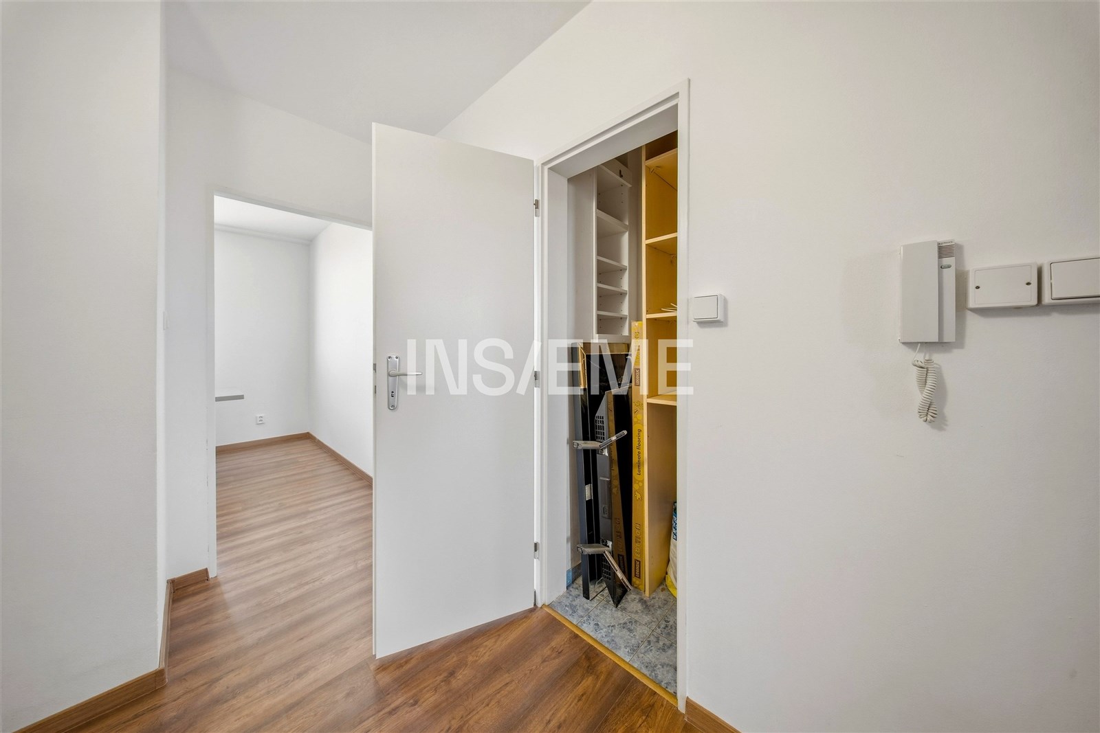 Chodba s dřevěnou podlahou a vestavěnými skříněmi, moderní interiér, světlé stěny, propojení do další místnosti, kvalitní materiály.